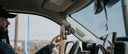 A man using his iPhone 14 that is secured to his car's grab handle with the new RAM form-fit holder. 